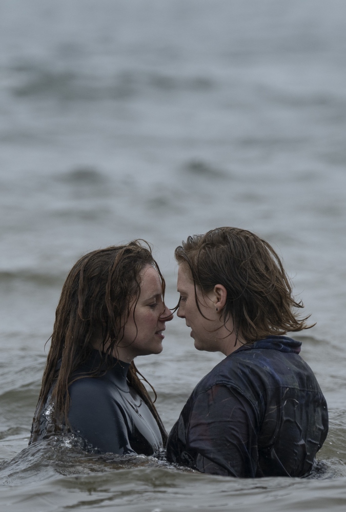 Two women embrace in the sea, face to face while surrounded by light waves